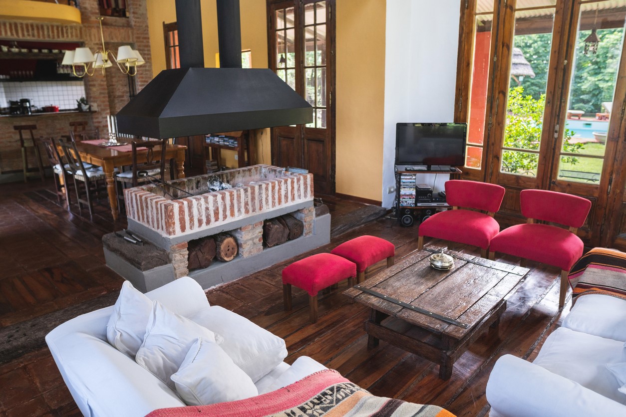 Rustic farmhouse living room showing a fireplace and white and red cushions and seats.